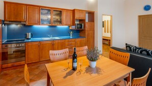 A modern kitchen with wooden cabinets, a blue countertop, and a dining area with a wooden table and chairs. - Base Camp 1 by Interhome (Desná v Jizerských horách)