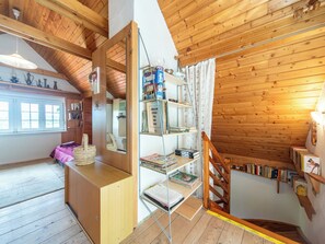 Ein Holzinnenraum mit einem Schlafplatz in der Höhe, einem kleinen Schreibtisch und einem Bücherregal voller Bücher.