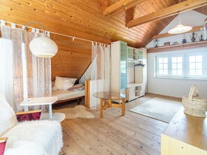L’intérieur chaleureux d’un chalet avec un lit en mezzanine, une table en verre et un plafond en bois rustique.