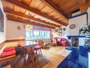 Une pièce chaleureuse avec des poutres apparentes, une table à manger, des chaises, un canapé et un poêle en faïence bleue.