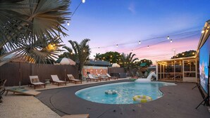 A backyard with a swimming pool, lounge chairs, and string lights.