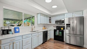 A modern kitchen with light blue cabinets, stainless steel appliances, and a wooden floor.