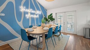 A dining area with a neon sign, blue chairs, and a large plant.