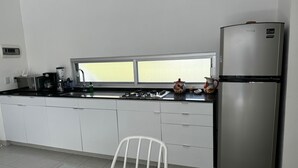 Uma cozinha moderna com armários brancos, uma geladeira de aço inoxidável, um fogão a gás e uma janela sobre a pia.