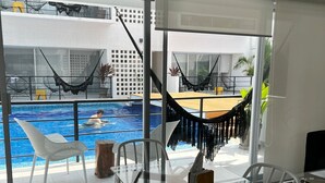 Quarto moderno com mesa e cadeiras de vidro, piscina com rede e vista para a cidade.