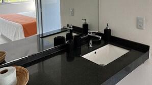 Uma casa de banho moderna com bancada preta, lavatório branco e um espelho grande.