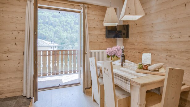 A wooden cabin with a dining area, a TV mounted on the wall, and a view of a forested area through the window. - Nice apartment in Lanzada (Lanzada)