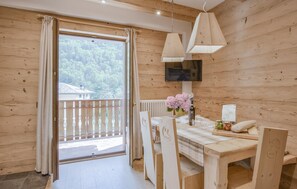 Uma cabana de madeira com área de jantar, uma TV fixada na parede e vista para uma área arborizada pela janela.