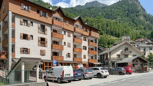 A multi-story hotel with balconies, a parking area, and a mountain backdrop. - Nice apartment in Lanzada (Lanzada)