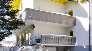 Ein zweistöckiges Haus mit Balkon, Steinstufen und einem gelben Markisenvorzelt.