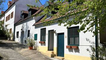 A row of white buildings with green doors and windows, a cobblestone street, and potted plants.