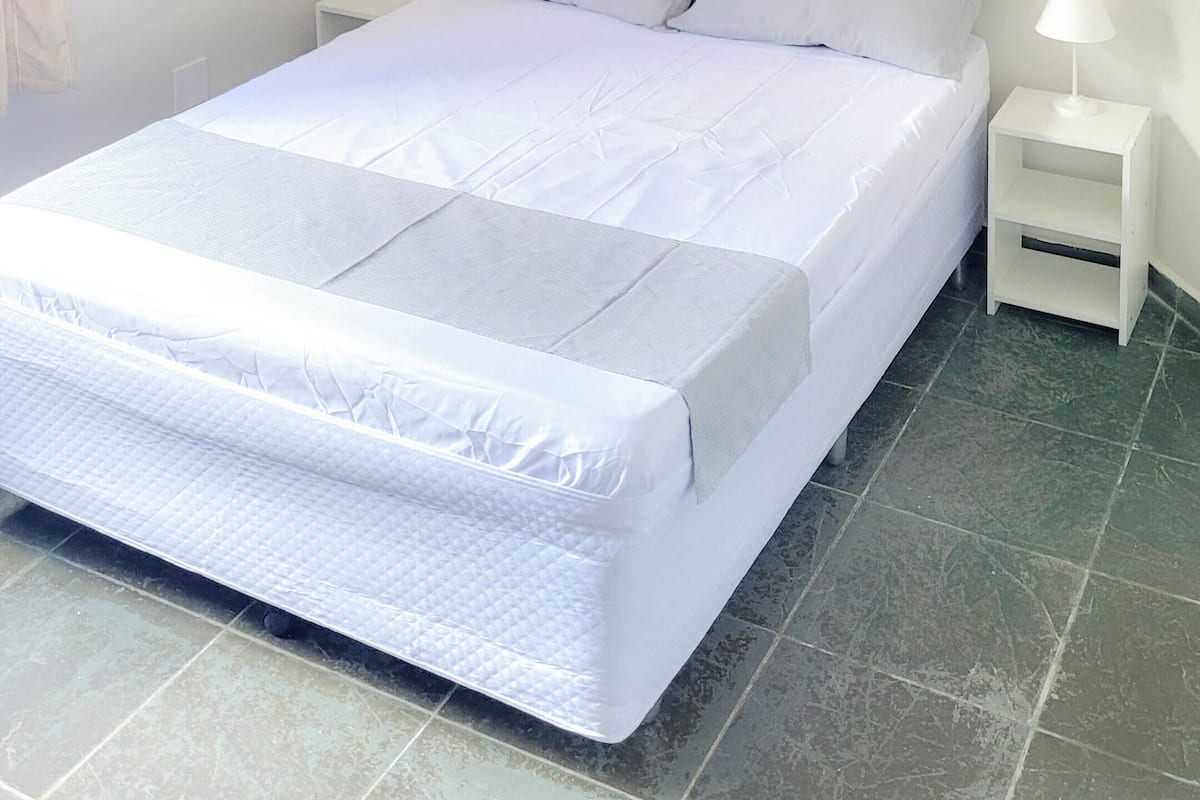 Un dormitorio con una cama, dos mesitas de noche, un ventilador de techo y una ventana con vidrio esmerilado.