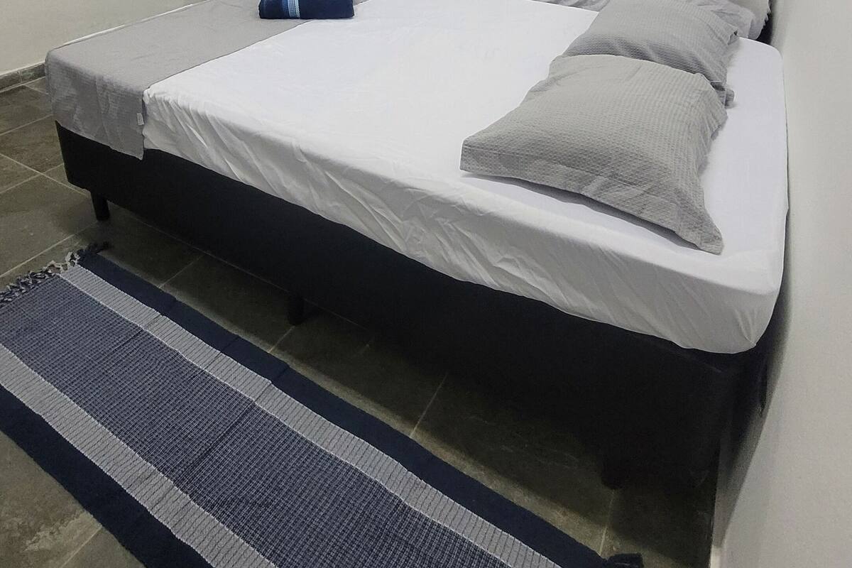 Un dormitorio con cama, mesita de noche, espejo y ventana con cortinas.