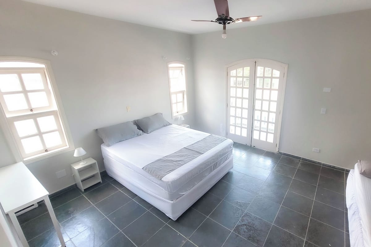 Un dormitorio con cama, mesita de noche, silla, ventilador de techo y ventana.