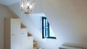 A bedroom with a sloped ceiling, a bed with floral bedding, a white wardrobe, and a chandelier.