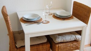 A dining table set with plates, a wine glass, and cutlery, flanked by wicker chairs with cushions.