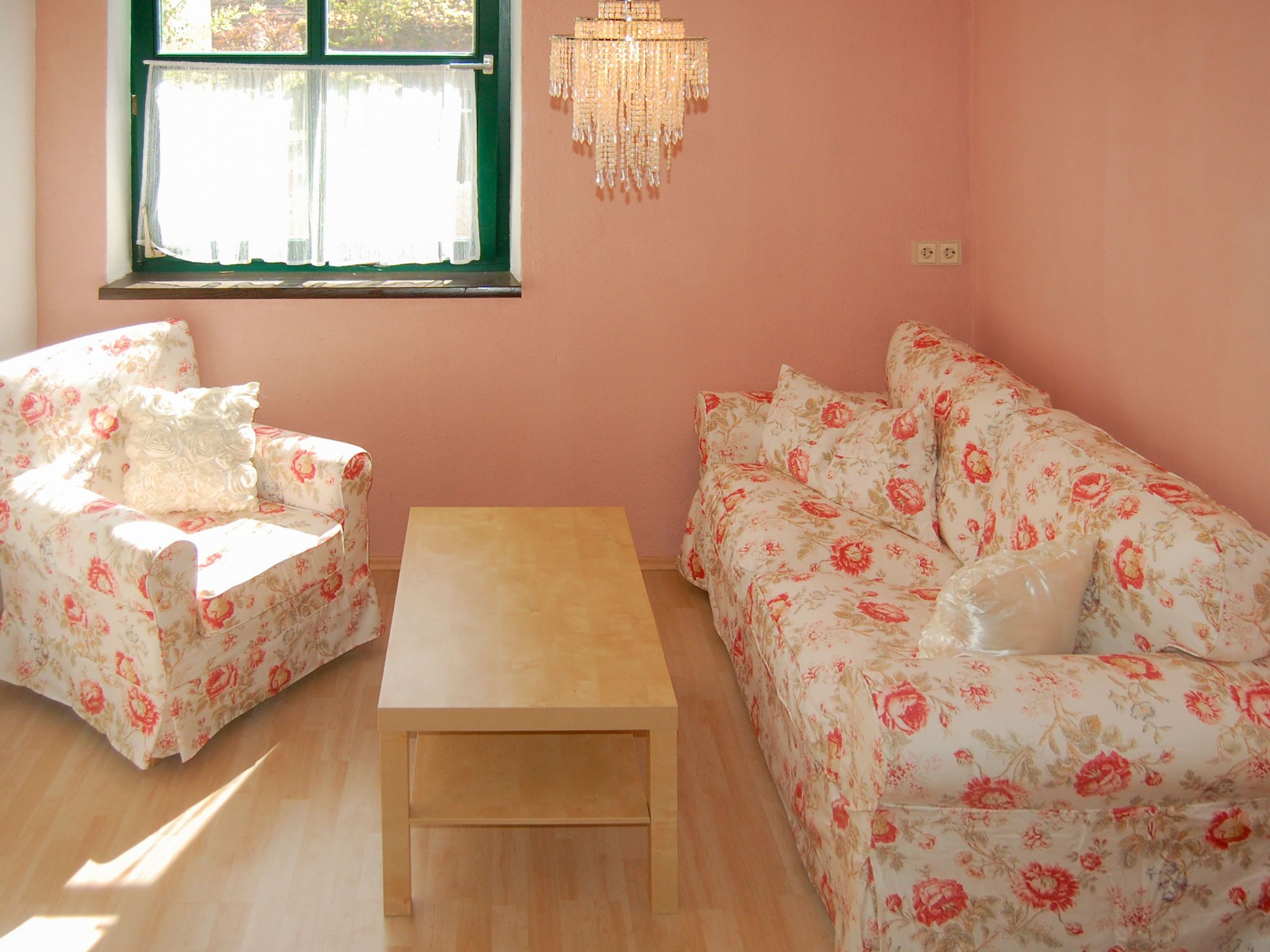 Ein Zimmer mit einem blumigem Sofa, einem passenden Sessel und einem Holztisch.