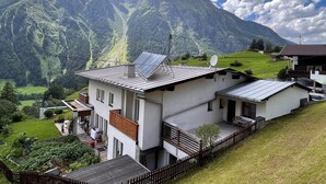 Ein modernes Haus mit Solaranlage, umzäunter Garten und Blick auf die Berge.