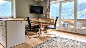 Ein Zimmer mit Esstisch, Stühlen, einem an der Wand befestigten Fernseher und Bergblick durch große Fenster.