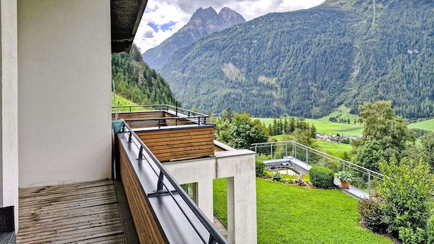 Ein Balkon mit Blick auf eine Berglandschaft, eine Holzterrasse und eine weiße Wand.