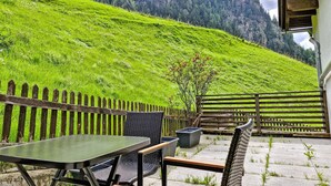 Un patio con mesa y sillas, una valla de madera y vistas a una ladera verde.