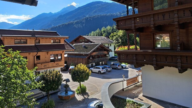 Un edificio de madera con balcón, zona de estacionamiento y vistas a la montaña.