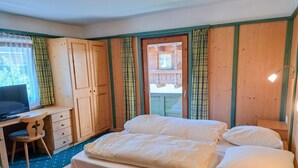 Un dormitorio con cama, escritorio y silla. Se ve una ventana con cortinas y vistas a un edificio.