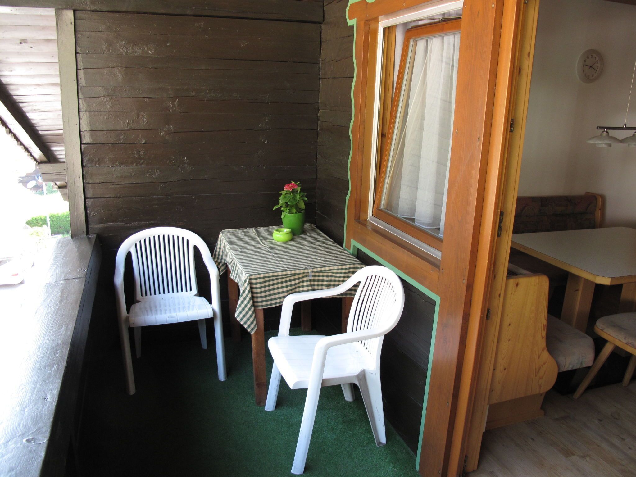 Une petite cabane en bois avec une table et deux chaises, une plante en pot et une fenêtre avec des rideaux.
