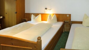 A hotel room with two single beds, wooden headboards, a nightstand with a lamp, and a wardrobe.
