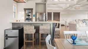A modern kitchen with stainless steel appliances, a bar area with wicker stools, and a dining table with a blue glass bowl.
