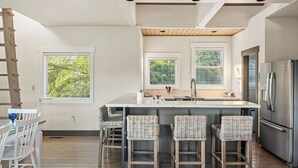 A modern kitchen with a central island, stainless steel appliances, and a dining area with wicker chairs.