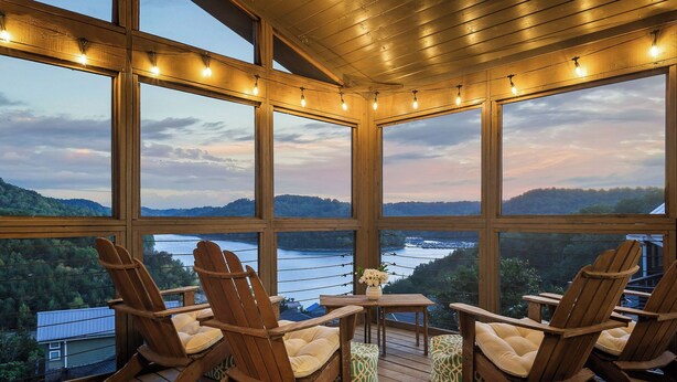 A wooden deck with Adirondack chairs and a small table, overlooking a river and hills.