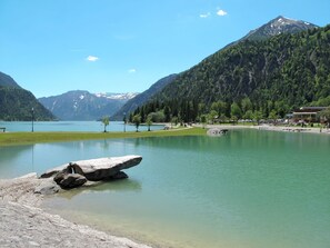 Een rustig stadsbeeld aan het meer, met een rotsachtige richel op de voorgrond, omgeven door weelderige begroeiing en bergen op de achtergrond.