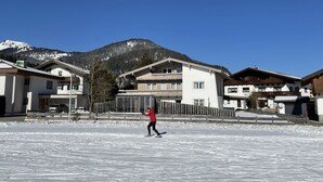 Una persona esquía de fondo sobre un sendero cubierto de nieve, con casas y una montaña al fondo.