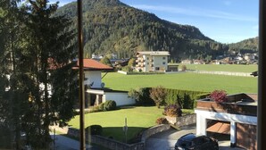 Vista desde una ventana de un edificio con un estacionamiento, un campo verde y una colina boscosa al fondo.