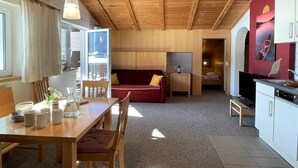 A cozy room with a wooden ceiling, a dining table with chairs, a red sofa, a small kitchen area, and a view of the outdoors. - Apartment Rofan by Interhome (Achensee)