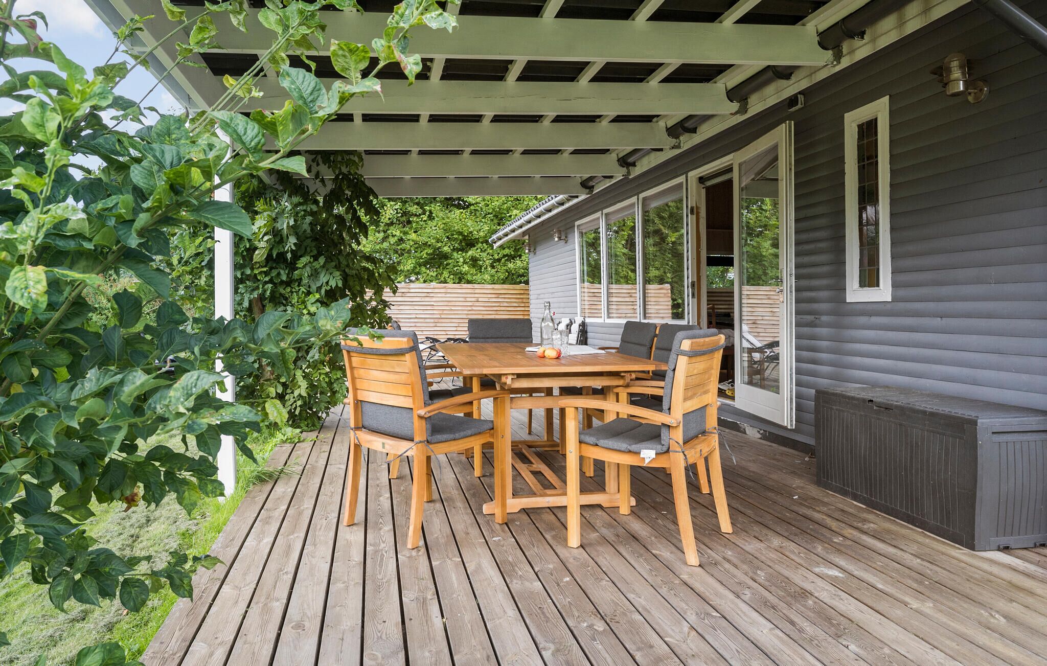 A wooden deck with a table and chairs, a pergola, and a house with a window.