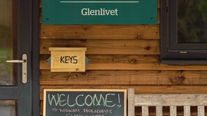 A wooden wall with a sign that reads "WIGWAM holidays Glenlivet" and a chalkboard sign saying "WELCOME! TO WIGWAM HOLIDAYS GLENLIVET!"
