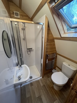 A compact bathroom with a shower, sink, toilet, and skylight.