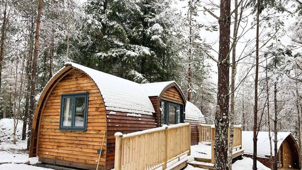 Een houten hut met een gebogen dak, omgeven door met sneeuw bedekte bomen.