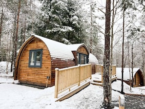 A wooden cabin with a curved roof, surrounded by snow-covered trees.