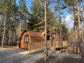 Een houten hut met een gebogen dak, omringd door hoge bomen.