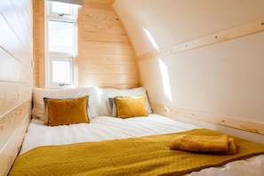 A cozy, sloped-roofed bedroom with a bed, pillows, and a blanket.