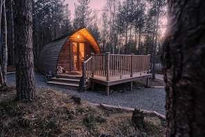 Een houten hutje met een terras en veranda, omringd door bomen.