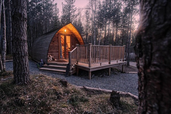 A wooden cabin with a deck and a porch, surrounded by trees.