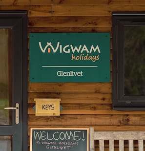 Een houten muur met een bord waarop staat 'WIGWAM holidays Glenlivet' en een schoolbord waarop staat 'WELKOM! BIJ WIGWAM HOLIDAYS GLENLIVET!'