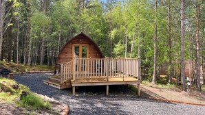 Een klein houten vakantiehuisje met een terras, omgeven door een bos.