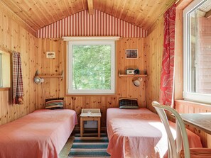 A cozy cabin room with two beds, a small table, a radio, and a window with a view of trees.