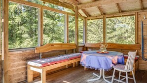 A wooden cabin with a bench, a table with a pitcher and glasses, and large windows overlooking a forest. - Dammeberg by Interhome (Karl Gustav)