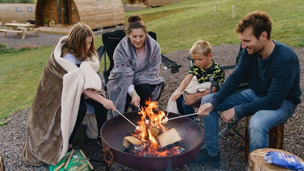A group of people roasting marshmallows around a campfire. - Rustic Coastal Cabin with Wood Fired Hot Tub (Cockburnspath)